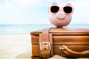 Pink piggy savings bank on a suitcase on the beach.